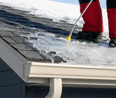 Ice dam removal technician using a steam wand to melt thick ice buildup on a residential roof in Aurora, IL